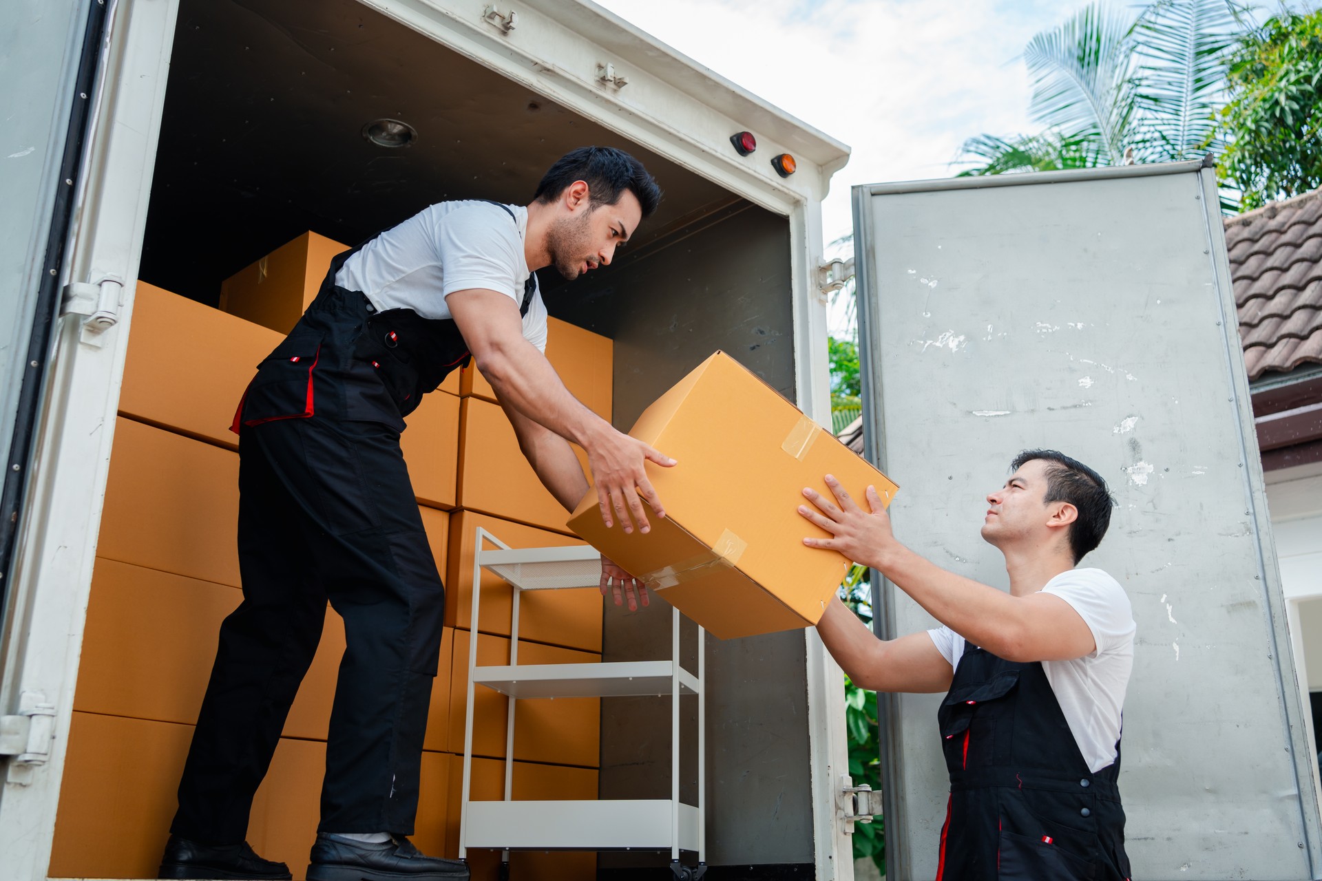 Unloading boxes and furniture from a pickup truck to a new house with service cargo two men movers worker in uniform lifting boxes. concept of Home moving and delivery.