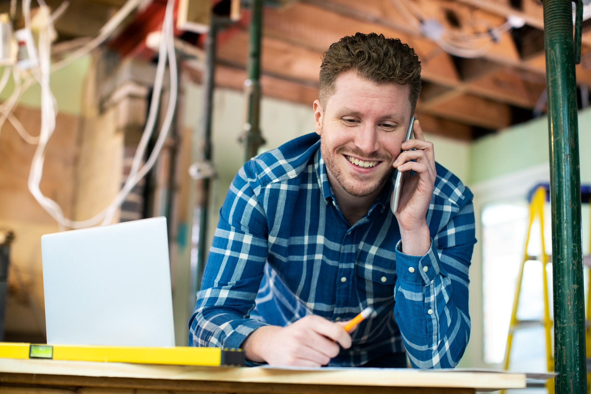 Architect Inside House Being Renovated Working On Plans Using Laptop And Talking On Cellphone